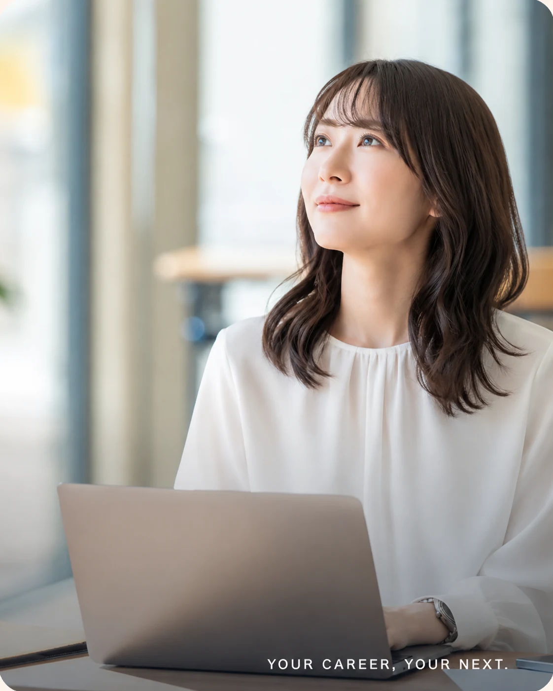 パソコンから顔を上げ、これからのキャリアを考える女性。YOUR CAREER, YOUR NEXT.